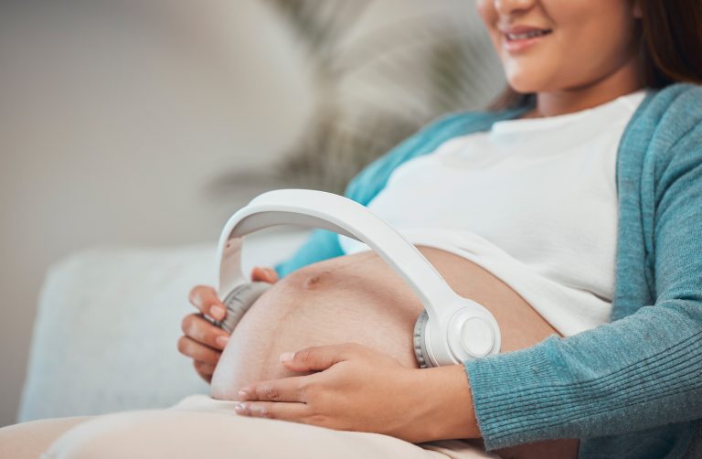 Pregnant woman, headphones and listening to music or podcast for zen, calm and peace with hands on .